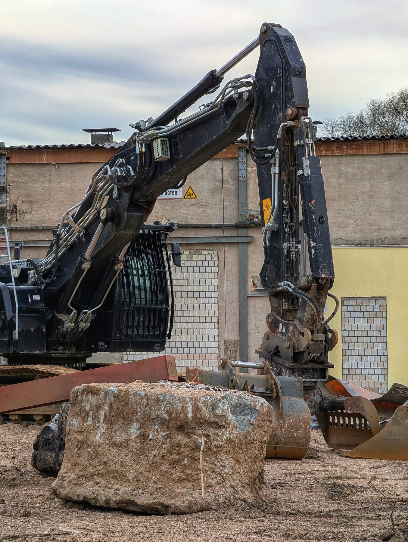 A tracked excavator with its arm raised over broken rock on a cleared plot.