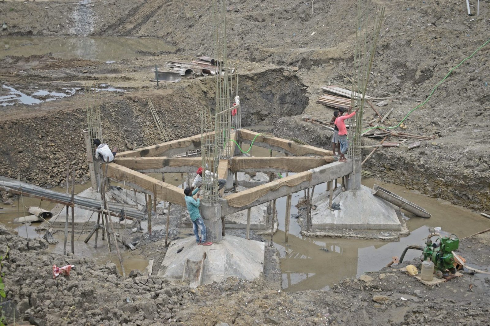Workers assembling timber formwork around steel reinforcement on a foundation.