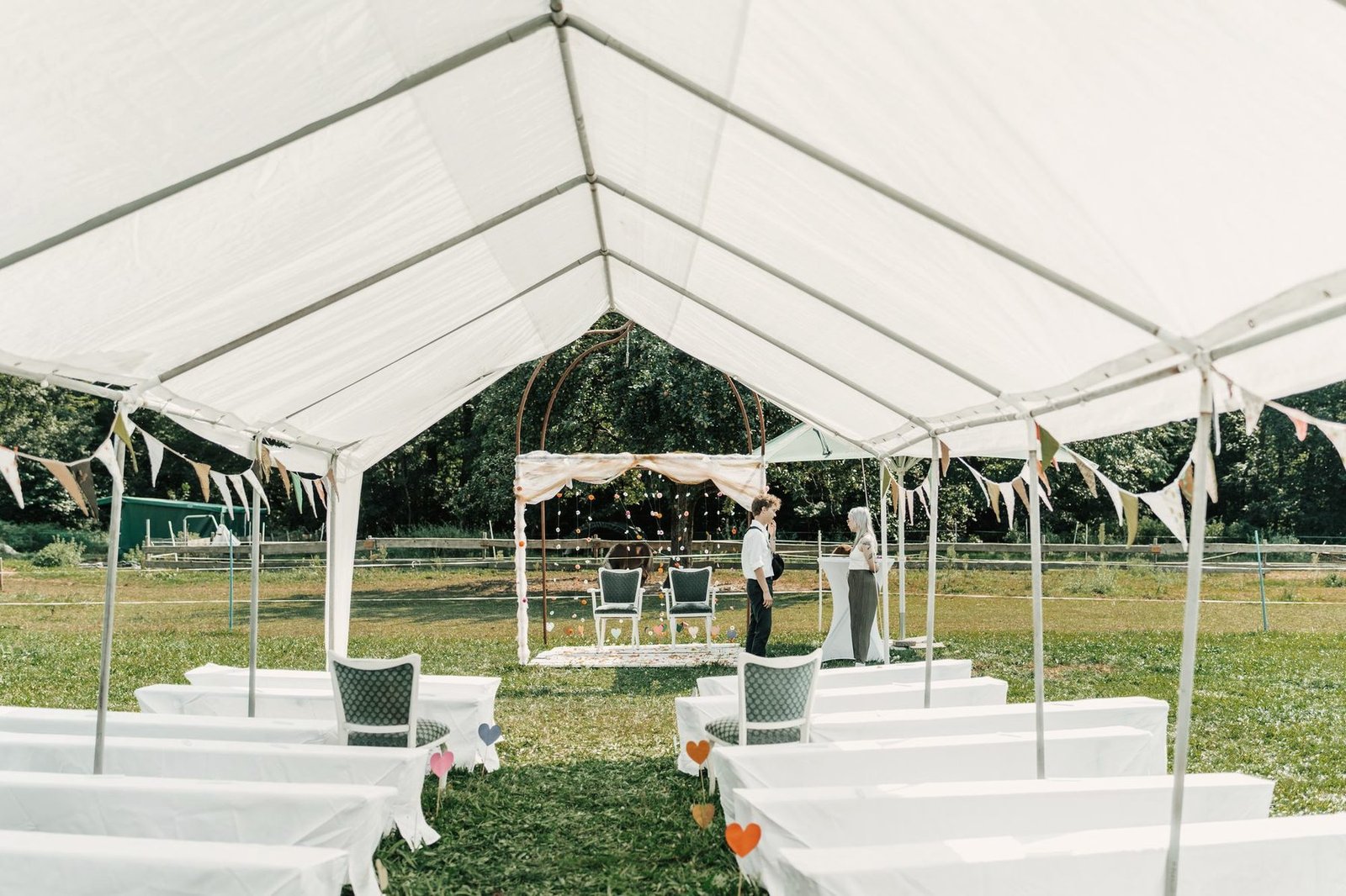 An empty white frame tent set up on grass with rows of chairs waiting for guests.
