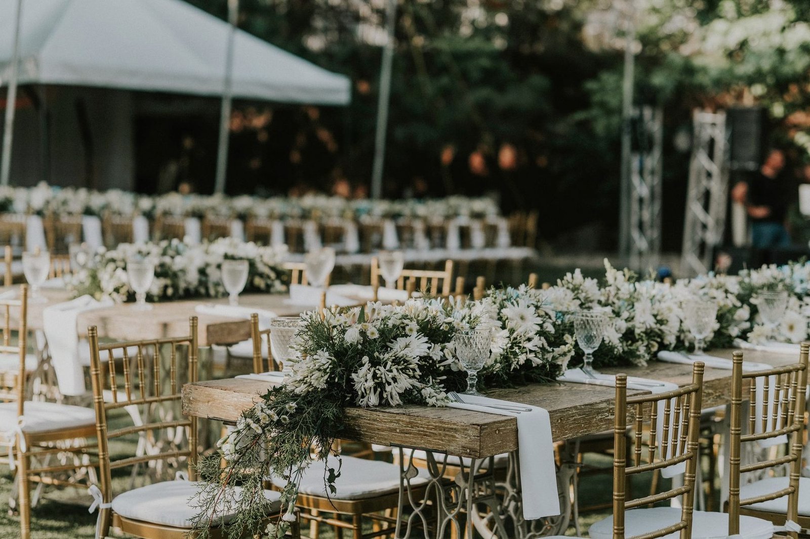 Tables dressed in white under a marquee with a floral centrepiece in the foreground.